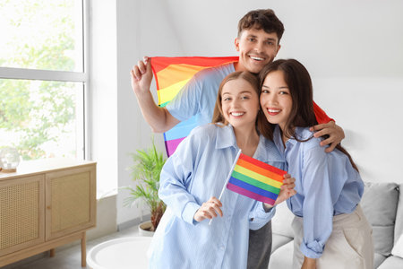 Young man with two women at LGBT flags at home. Polyamory conceptの写真素材