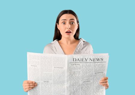 Shocked young woman in pajamas reading newspaper on blue backgroundの写真素材