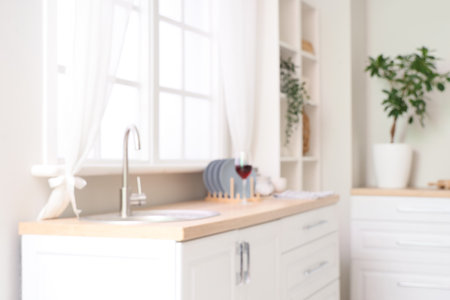 Blurred view of light kitchen with white counters, sink and windowの写真素材