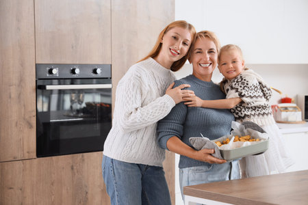 Young woman with her little daughter and mother holding baked potato near oven in kitchen