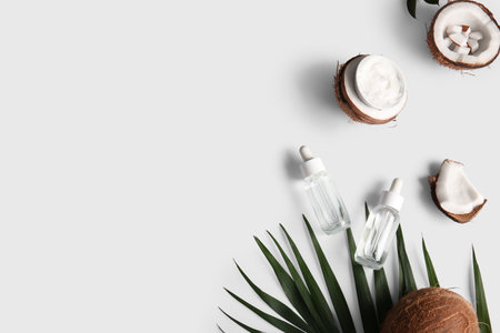 Bottles of coconut cosmetic oil and bowl of cream with palm leaf on gray backgroundの写真素材