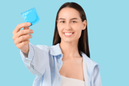Young woman with condom on blue background, closeupの写真素材