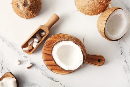 Wooden board and scoop with cut fresh coconut on white background