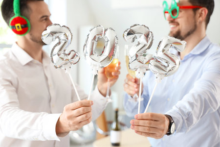 Male colleagues with figure 2025 celebrating New Year at party in office, closeup