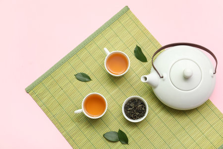 Cups and teapot of hot tea with dried leaves on pink backgroundの写真素材