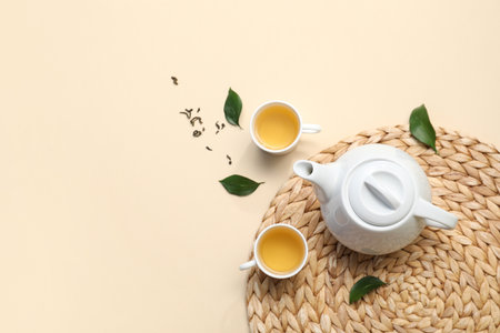 Cups and teapot of hot tea with dried leaves on beige backgroundの写真素材