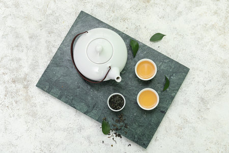 Bowls and teapot of hot tea with dried leaves on white background