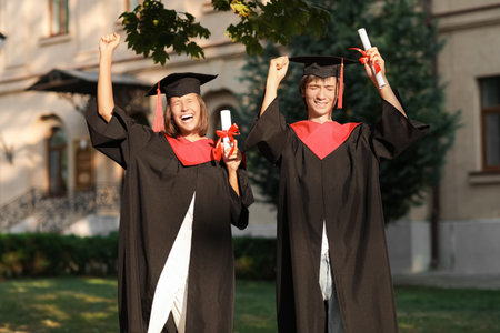 Happy graduated students with diplomas outdoors