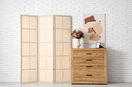 Folding screen, picture and vase with wild flowers on chest of drawers in room