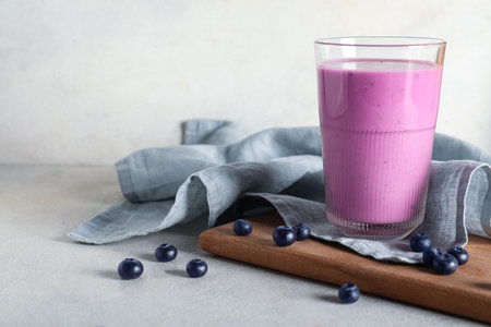 Glass of fresh blueberry smoothie and wooden board with berries on white backgroundの写真素材