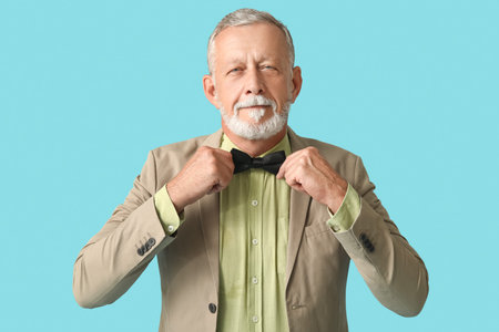 Handsome mature man with stylish bow tie on blue background