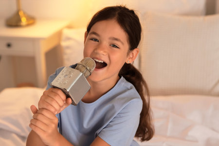 Little girl with microphone singing in bedroom at night, closeupの写真素材