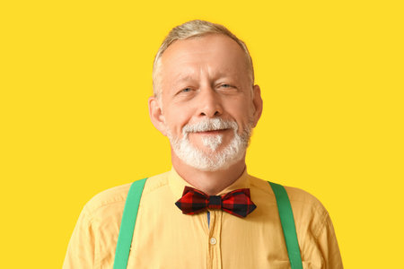 Handsome happy mature man with stylish bow tie on yellow background