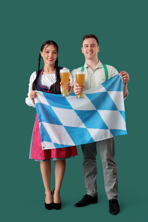 Young happy couple in traditional German clothes with glasses of beer and Bavarian flag on green backgroundの写真素材
