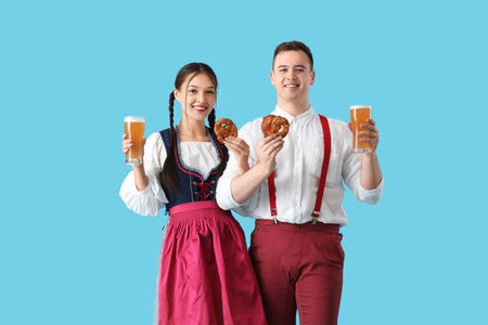 Young happy couple in traditional German clothes with pretzels and glasses of beer on blue backgroundの写真素材
