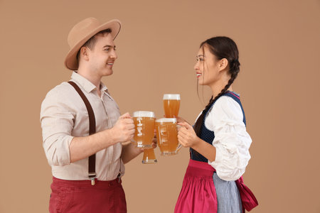 Young happy couple in traditional German clothes with glasses and mugs of beer on beige backgroundの写真素材