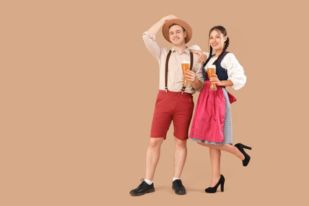 Young happy couple in traditional German clothes with glasses of beer on beige backgroundの写真素材