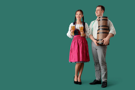 Young happy couple in traditional German clothes with barrels and glasses of beer on green backgroundの写真素材