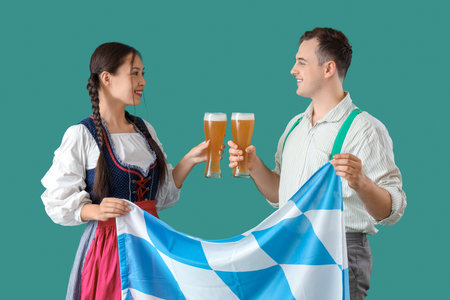 Young happy couple in traditional German clothes with glasses of beer and Bavarian flag on green backgroundの写真素材