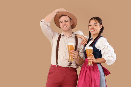 Young happy couple in traditional German clothes with glasses of beer on beige backgroundの写真素材