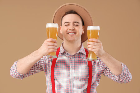 Handsome young happy man in traditional German clothes with glasses of beer on beige backgroundの写真素材