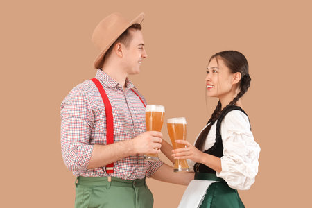 Young happy couple in traditional German clothes with glasses of beer on beige backgroundの写真素材