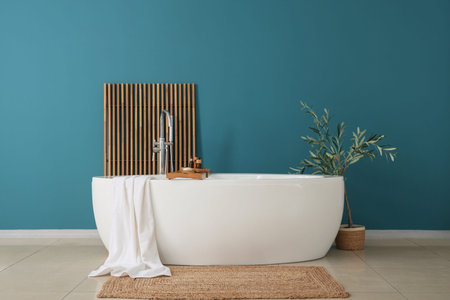 Bathtub with towel, screen and decorative tree in interior of bathroom