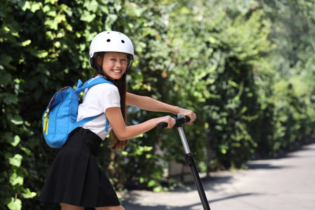 Cute schoolgirl in helmet with electric scooter outdoorsの写真素材
