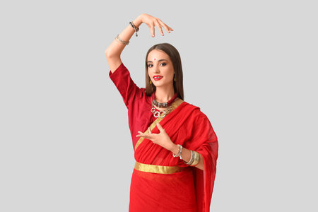 Beautiful young happy Indian woman in sari dancing on gray backgroundの写真素材