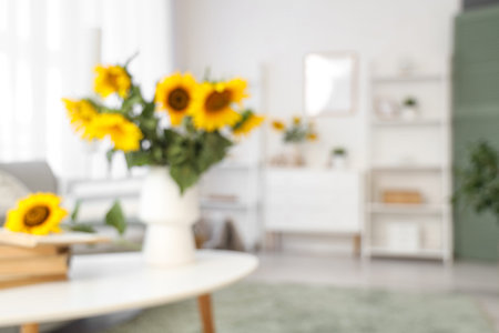 Blurred view of vase with sunflowers and books on table in light living roomの写真素材