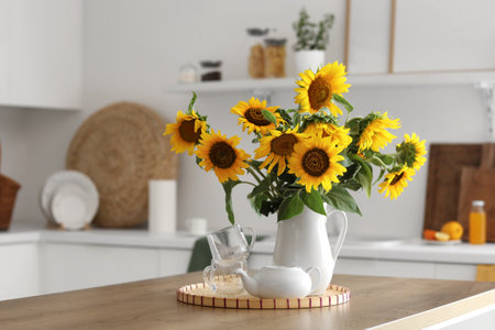 Vase with sunflowers, teapot and cups on dining table in light kitchenの写真素材