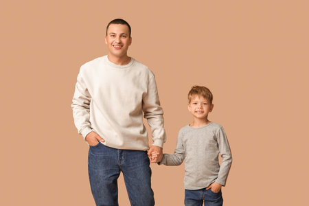Happy father and his little son holding hands on beige backgroundの写真素材