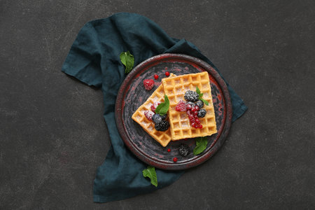 Plate of sweet Belgian waffles with different fresh berries and mint on black backgroundの写真素材
