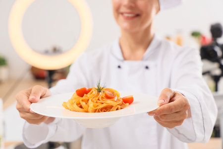 Mature female chef with tasty pasta recording cooking video class in kitchen, closeupの写真素材