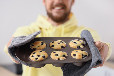 Young man holding baking dish with tasty muffins in kitchen, closeupの写真素材