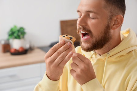 Young man eating tasty muffin in kitchen, closeup