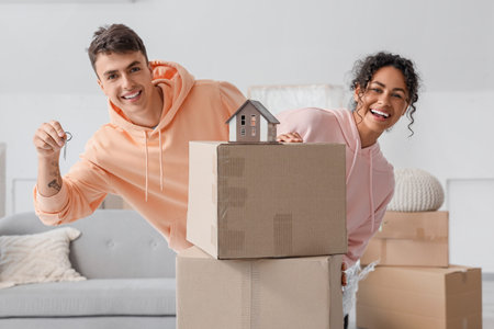 Young couple with keys from their new flat and boxes in room on moving day