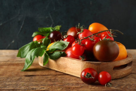 Tomatoes on wooden tray on table against black background. Closeupの写真素材