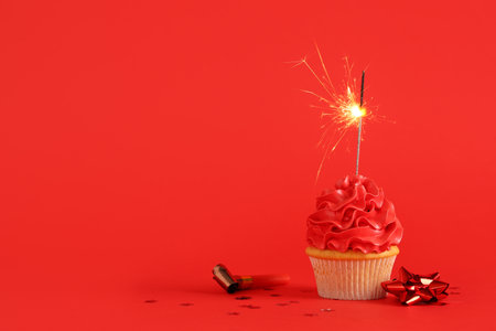 Sweet Birthday cupcake with sparkler and party whistle on red backgroundの写真素材