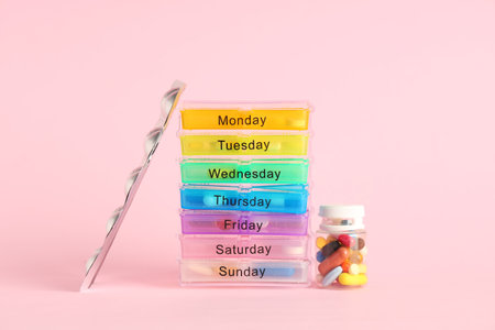 Pack of plastic pill organizers, blister and bottle with pills on pink backgroundの写真素材