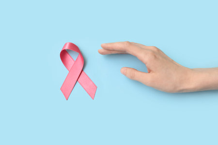 Female hand with pink silk ribbon on blue background. Breast cancer concept