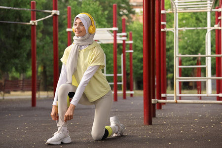 Sporty Muslim woman in headphones tying shoelaces outdoorsの写真素材