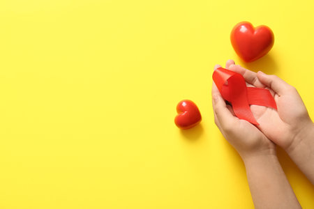 Female hands with red ribbon and hearts on yellow background. Blood Cancer Awareness Monthの写真素材