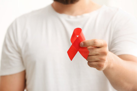 Young man with red ribbon on white background, closeup. Blood Cancer Awareness Month