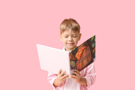 Cute little boy reading book on pink backgroundの写真素材