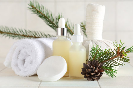 Composition with bottles of essential oil, spa accessories and coniferous branches on light tile backgroundの写真素材
