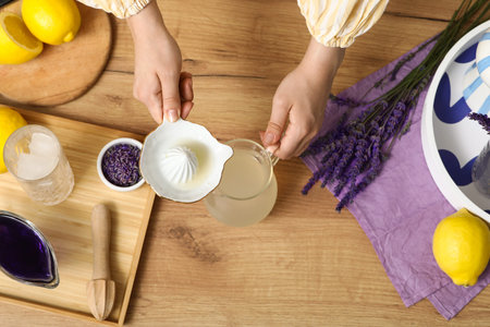 Woman pouring lemon juice from juicer into jug for preparing lavender lemonade on wooden table