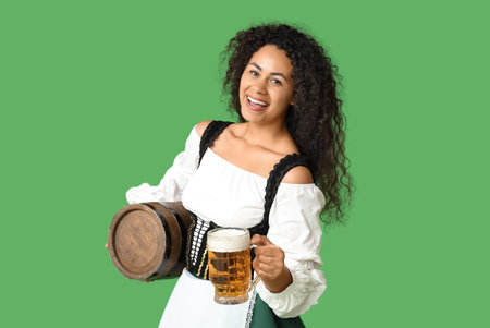 Happy African-American woman with beer on green background. Octoberfest celebration