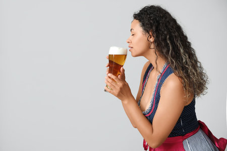 Happy African-American woman with beer on gray background. Octoberfest celebration