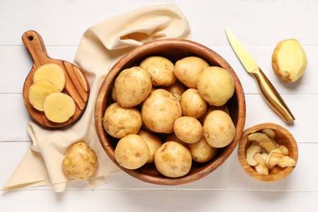 Bowl and board with raw potatoes on white wooden backgroundの写真素材